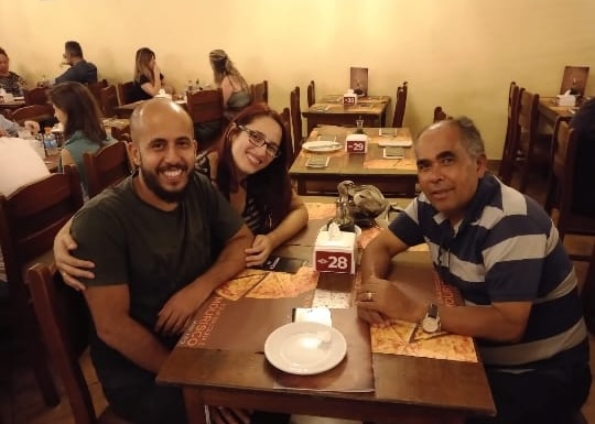 Ivan sorrindo em uma pizzaria com seu filho e sua nora, Karen